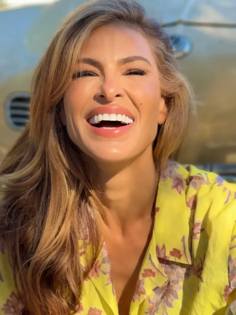 Eva Mendes laughing, with honey-brown waves over one shoulder and glossy pink lips